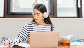 Woman with headphones on laptop taking notes