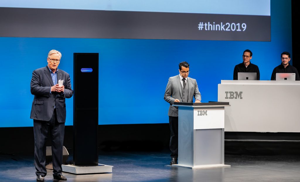 AIシステムであるIBM Project Debater（中央）とディベートの世界チャンピオンのハリシュ・ナタラジャン（右）が、「幼稚園/保育園に助成金を交付すべきである。」という論題について討論している様子